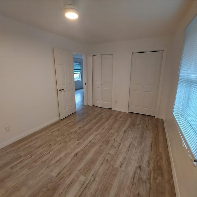 unfurnished bedroom with multiple closets and light wood-type flooring