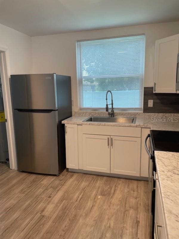 kitchen with sink, light hardwood / wood-style flooring, stainless steel refrigerator, electric stove, and white cabinets