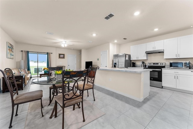 kitchen with light tile patterned floors, appliances with stainless steel finishes, a kitchen island, ceiling fan, and white cabinets