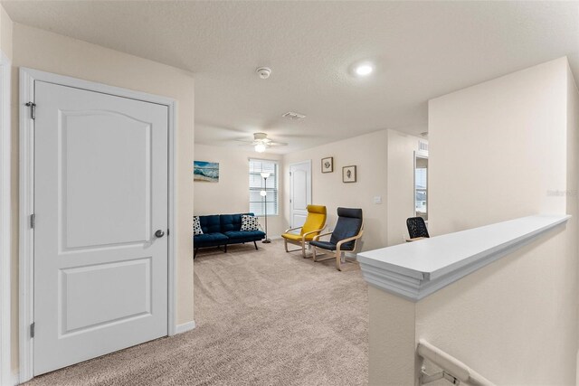 sitting room featuring ceiling fan, light colored carpet, and a textured ceiling