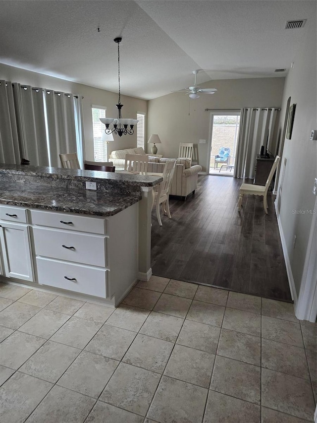 kitchen featuring pendant lighting, lofted ceiling, dark stone countertops, white cabinets, and light tile patterned flooring