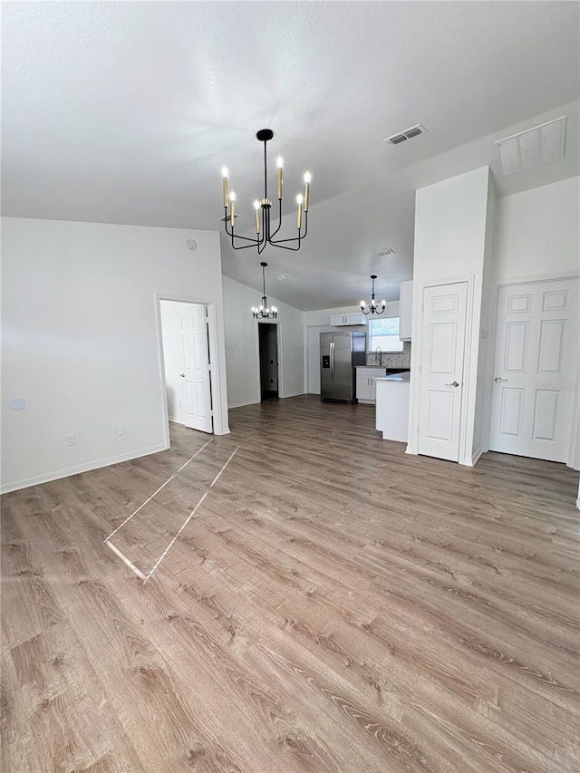 unfurnished living room with vaulted ceiling, light hardwood / wood-style floors, and a chandelier