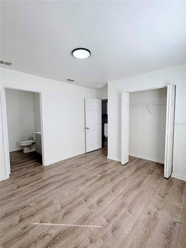 unfurnished bedroom featuring connected bathroom, a textured ceiling, light hardwood / wood-style floors, and a closet