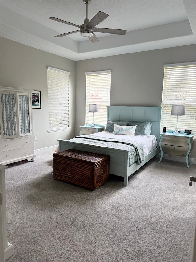 carpeted bedroom featuring ceiling fan and a tray ceiling