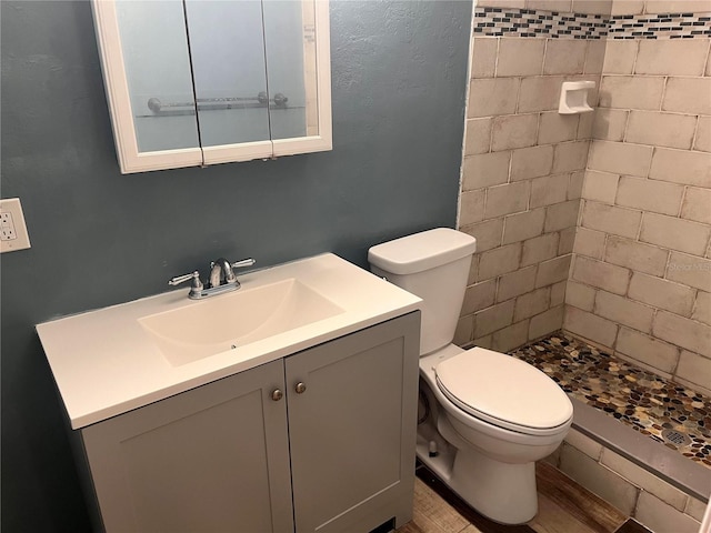 bathroom with tiled shower, vanity, toilet, and wood-type flooring