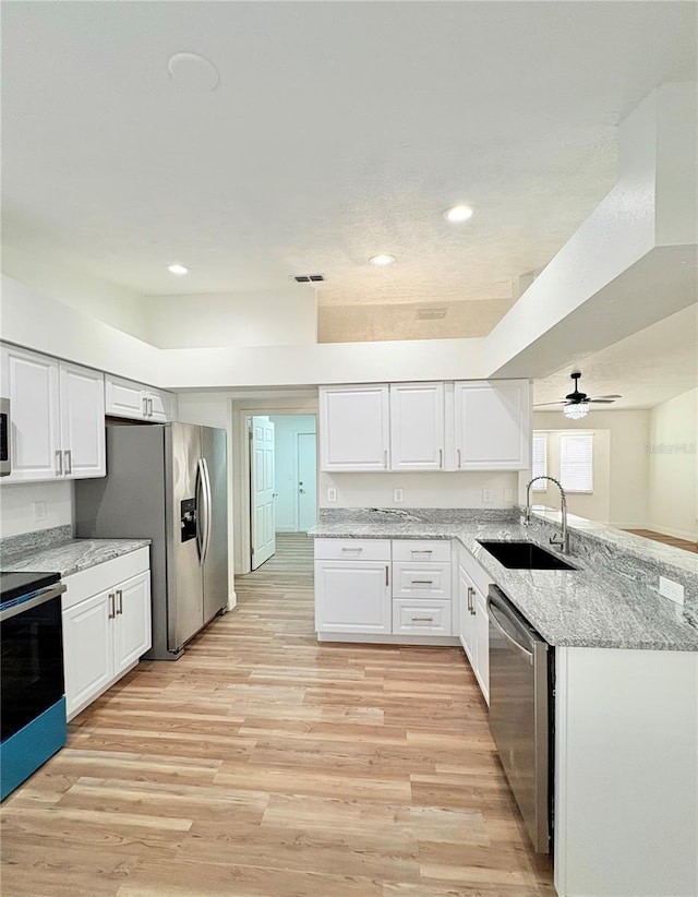 kitchen featuring sink, appliances with stainless steel finishes, light stone counters, white cabinets, and kitchen peninsula