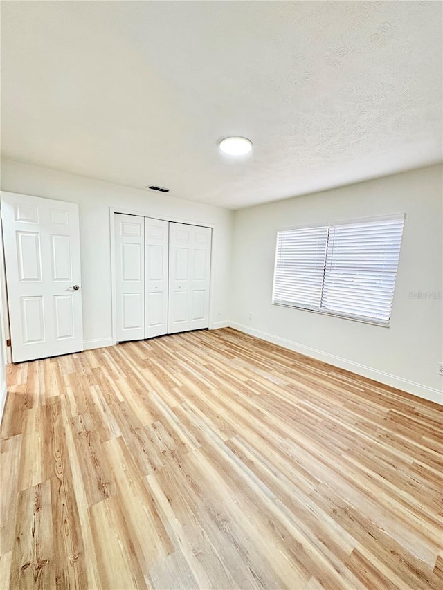 unfurnished bedroom with a textured ceiling, light wood-type flooring, and a closet