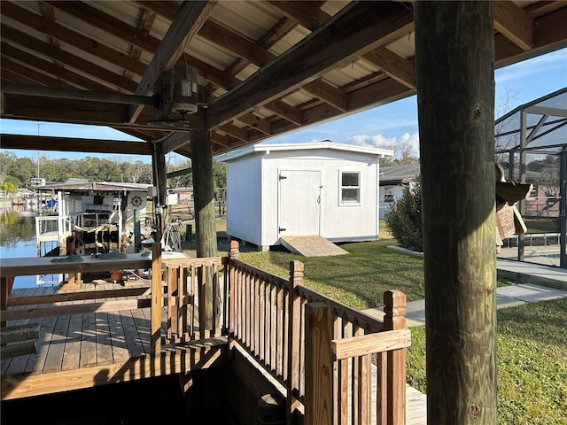 deck with a yard, a water view, a dock, glass enclosure, and a storage shed