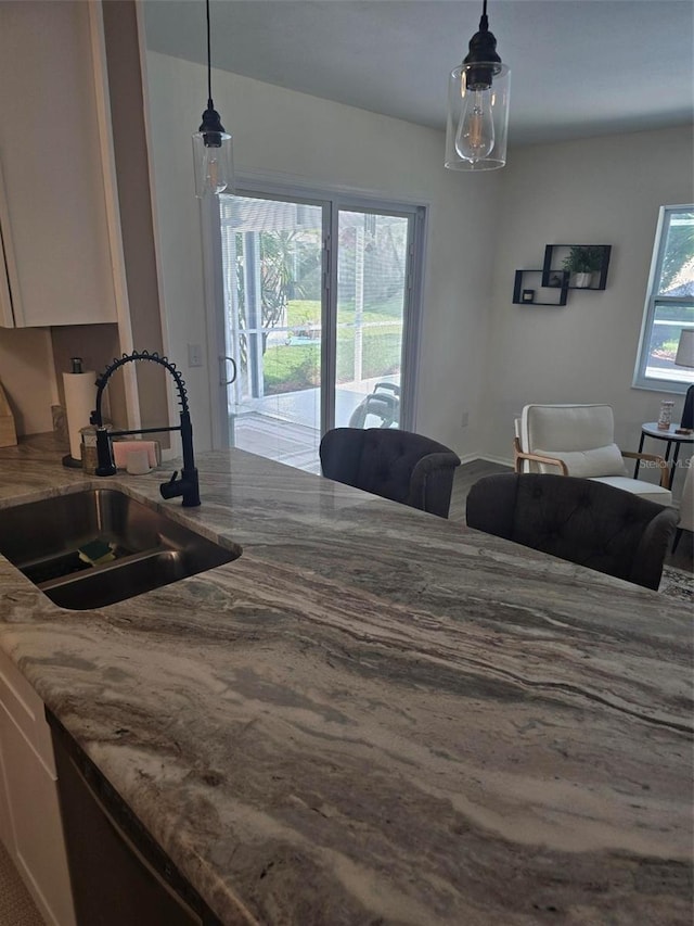 kitchen featuring sink, light stone countertops, hanging light fixtures, and white cabinets