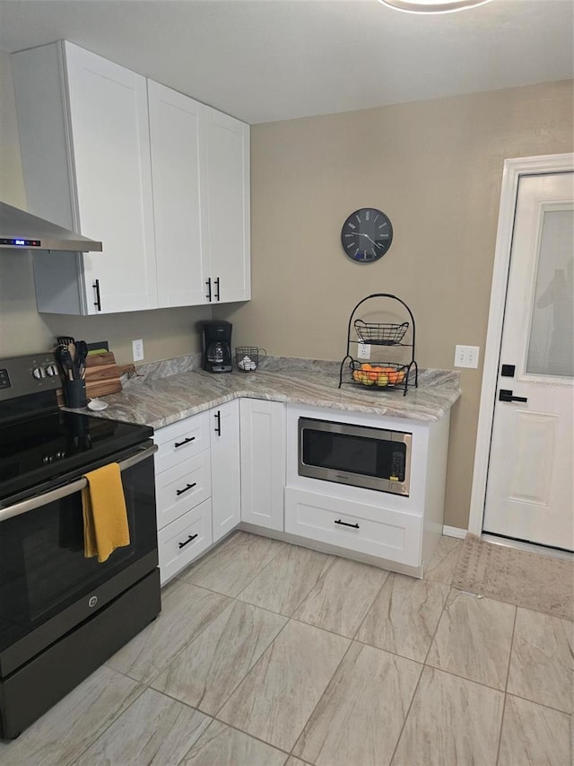 kitchen with wall chimney range hood, black range with electric stovetop, stainless steel microwave, and white cabinetry