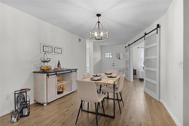 dining room featuring a barn door, light wood-style floors, a chandelier, and baseboards