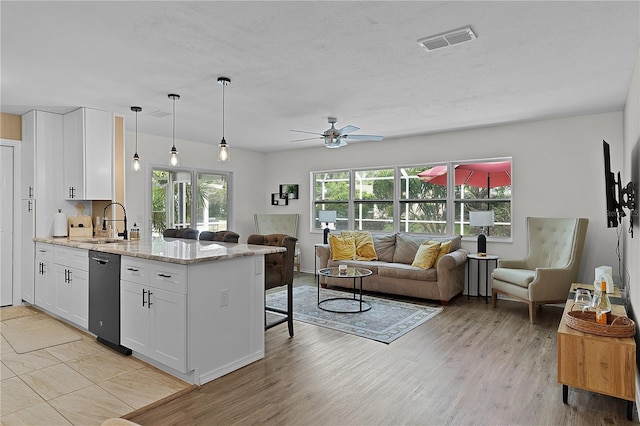 kitchen featuring black dishwasher, open floor plan, a sink, a kitchen bar, and white cabinetry