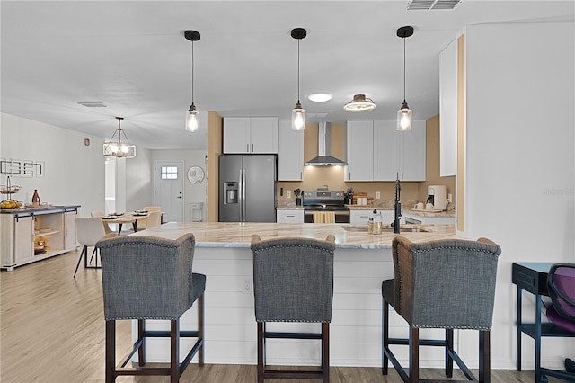 kitchen with stainless steel appliances, wall chimney exhaust hood, a breakfast bar, light wood finished floors, and white cabinets