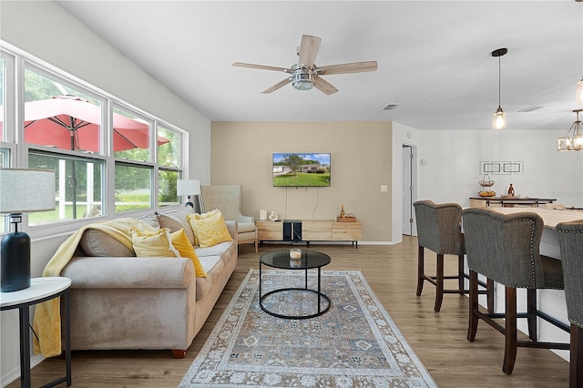 living area featuring plenty of natural light, ceiling fan, wood finished floors, and a chandelier
