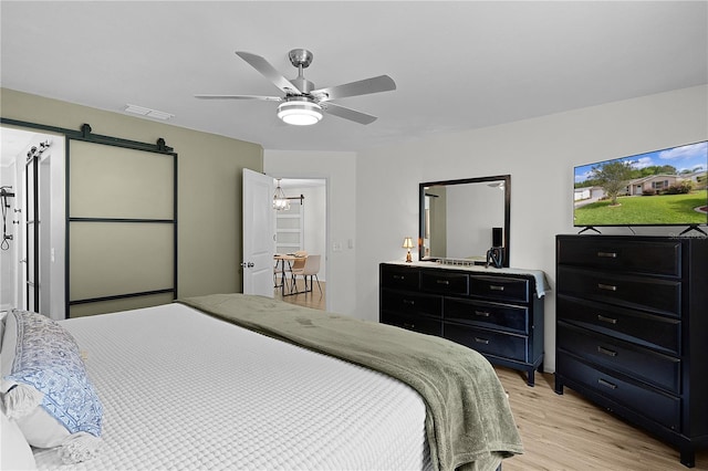 bedroom with light wood-style floors, a barn door, and a ceiling fan