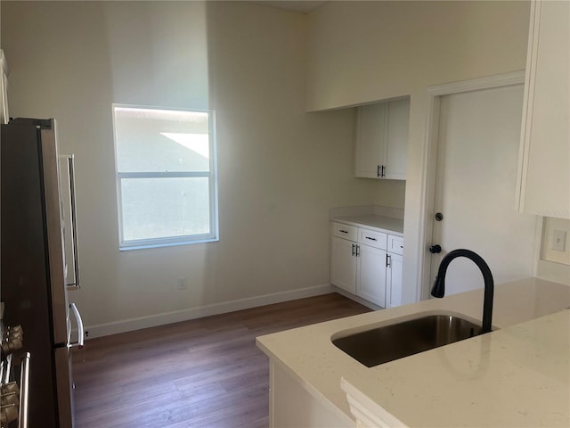 kitchen featuring sink, stainless steel refrigerator, white cabinetry, light stone counters, and light wood-type flooring