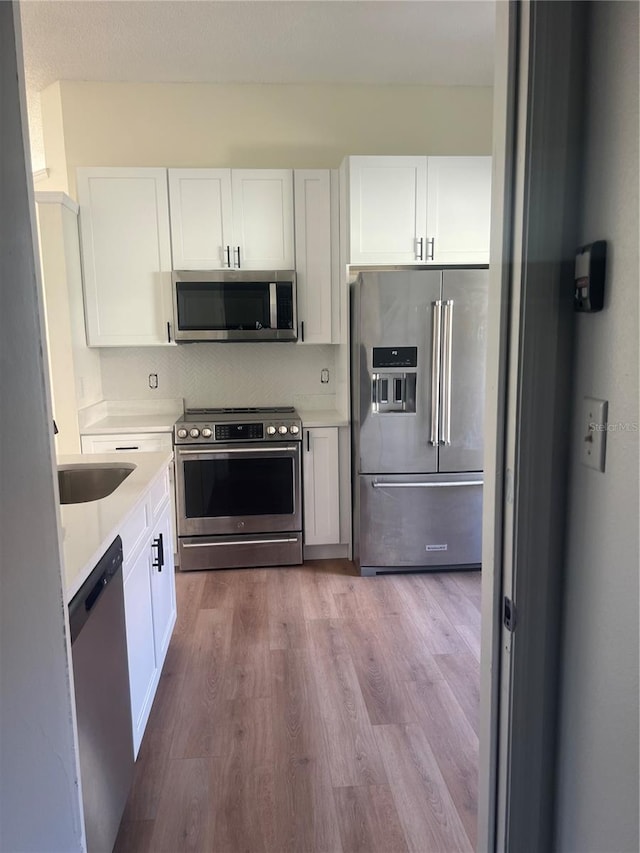 kitchen featuring white cabinetry, wood-type flooring, sink, decorative backsplash, and stainless steel appliances