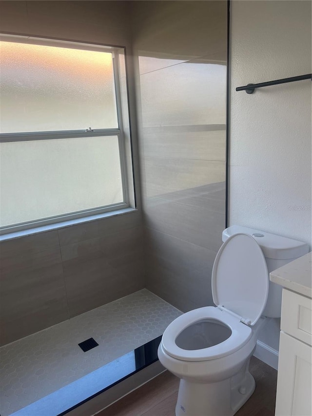 bathroom featuring hardwood / wood-style flooring, tiled shower, vanity, and toilet