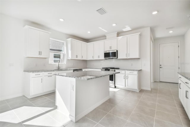 kitchen featuring stainless steel appliances, light stone countertops, white cabinets, a kitchen island, and decorative backsplash