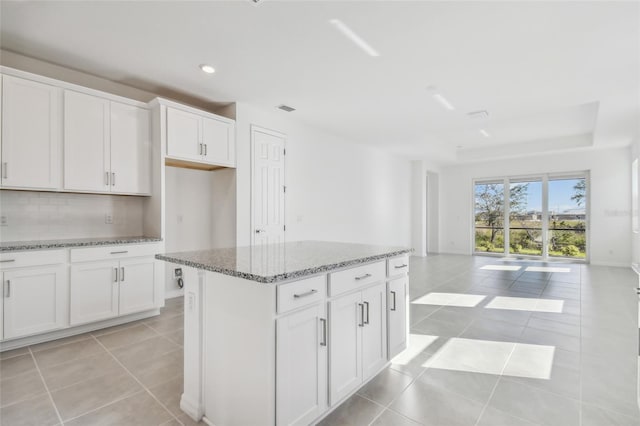 kitchen featuring light stone countertops, light tile patterned floors, a kitchen island, and white cabinets