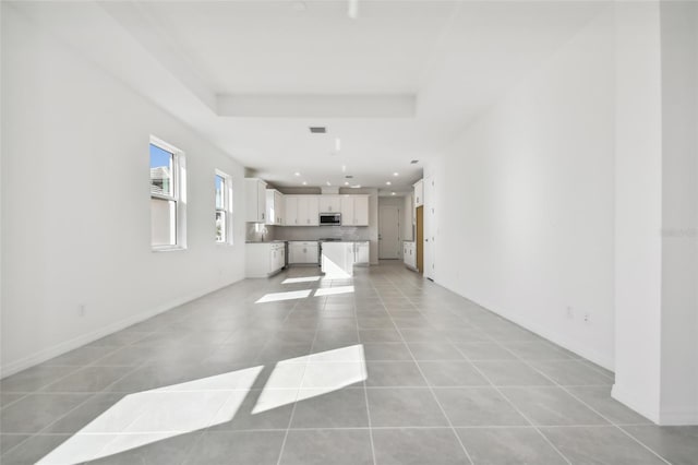 unfurnished living room with light tile patterned flooring and a tray ceiling