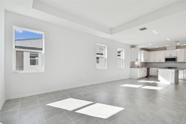 unfurnished living room with a raised ceiling, sink, and light tile patterned floors