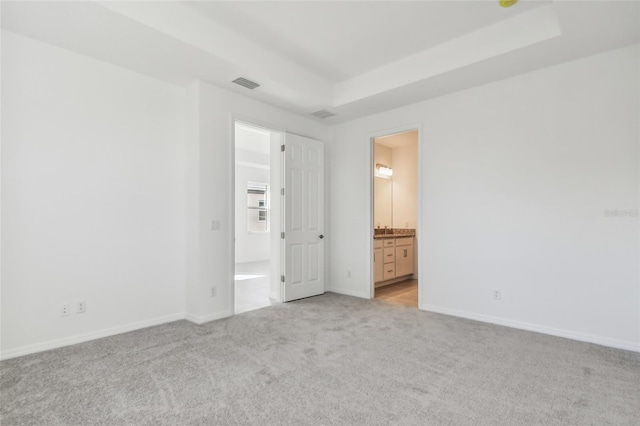 unfurnished bedroom featuring light carpet, connected bathroom, and a tray ceiling