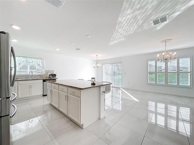 kitchen with an inviting chandelier, a kitchen island, stone counters, pendant lighting, and stainless steel appliances