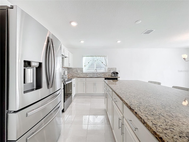 kitchen featuring sink, stainless steel appliances, light stone counters, tasteful backsplash, and white cabinets