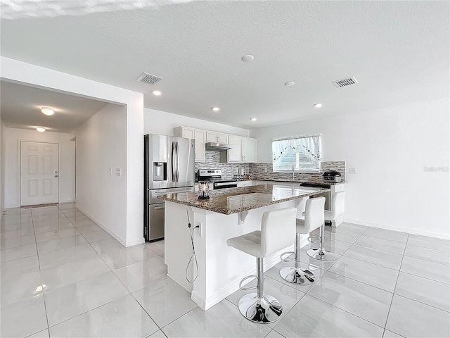 kitchen with white cabinetry, dark stone countertops, appliances with stainless steel finishes, a kitchen island, and backsplash