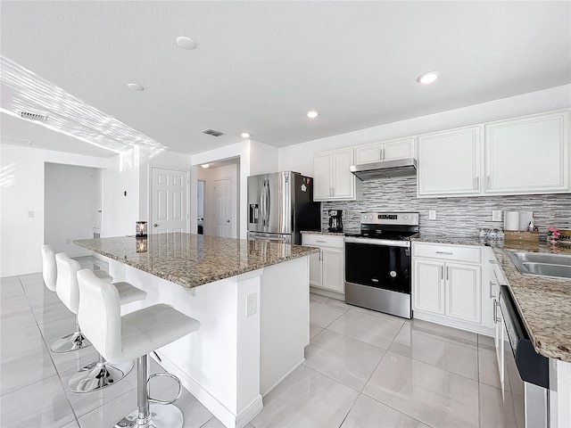 kitchen with appliances with stainless steel finishes, white cabinetry, a kitchen island, decorative backsplash, and dark stone counters