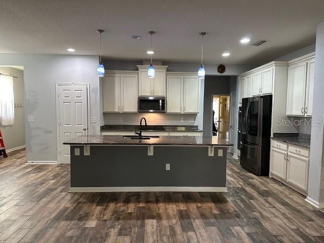 kitchen featuring an island with sink, black refrigerator, and decorative light fixtures