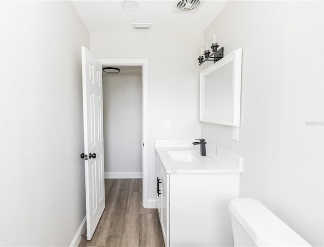 bathroom featuring visible vents, toilet, vanity, wood finished floors, and baseboards
