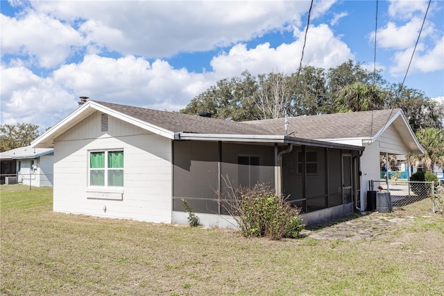 view of home's exterior with a sunroom, roof with shingles, fence, and a yard