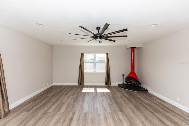 empty room featuring a wood stove, light wood finished floors, and baseboards
