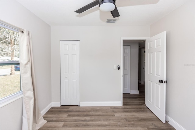 unfurnished bedroom with ceiling fan, wood finished floors, visible vents, baseboards, and a closet