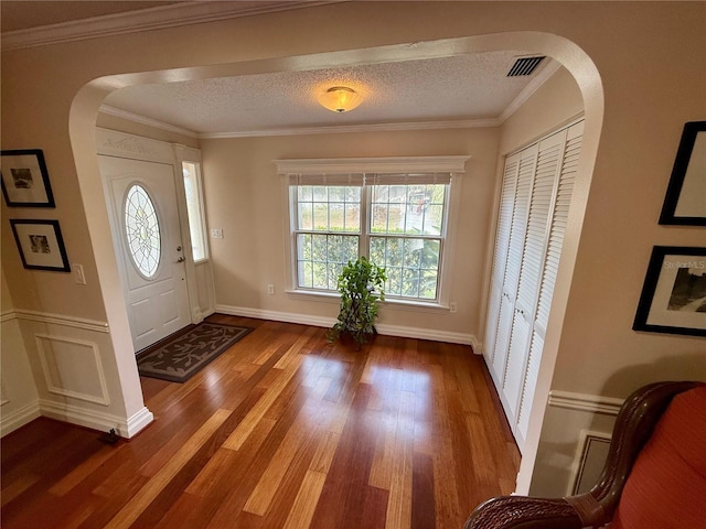 entrance foyer with a textured ceiling, arched walkways, wood finished floors, and visible vents