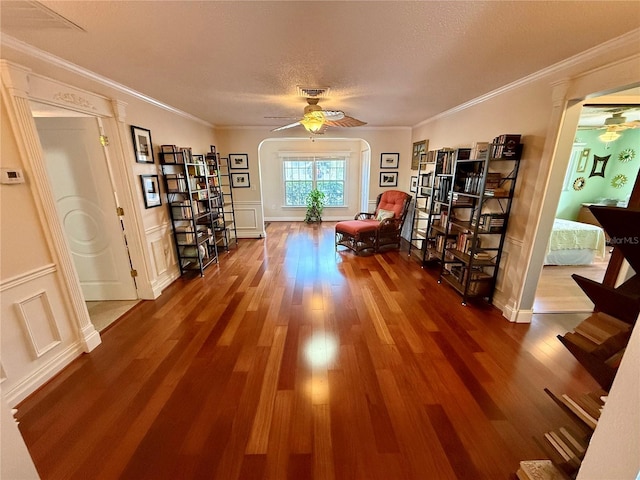 living area with visible vents, ornamental molding, wainscoting, ceiling fan, and wood finished floors