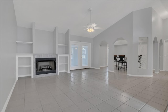 unfurnished living room with built in shelves, a ceiling fan, baseboards, and light tile patterned floors