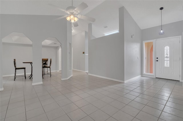 entrance foyer featuring light tile patterned floors, baseboards, arched walkways, and high vaulted ceiling