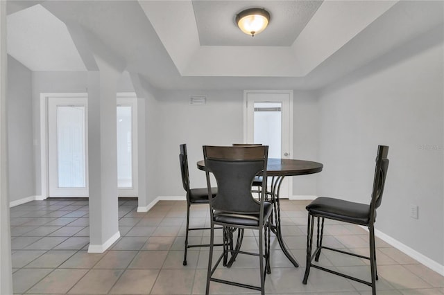 dining area with a tray ceiling, tile patterned floors, and baseboards