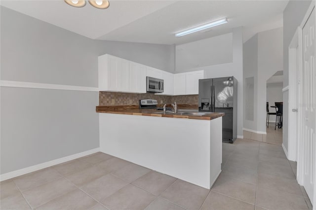 kitchen with stainless steel appliances, a peninsula, white cabinetry, vaulted ceiling, and tasteful backsplash