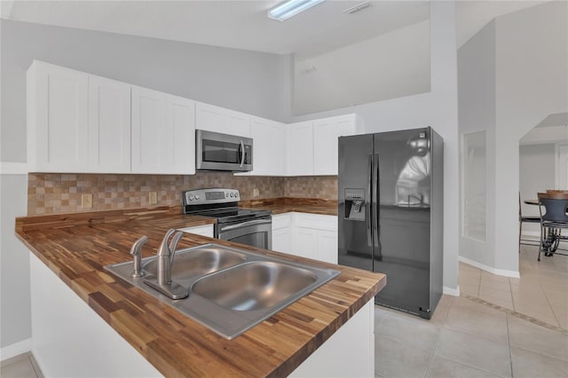 kitchen with a sink, stainless steel appliances, wood counters, and white cabinetry