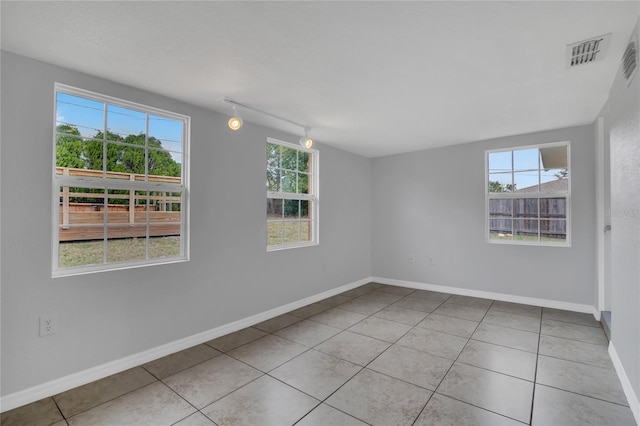 empty room with a healthy amount of sunlight, baseboards, visible vents, and light tile patterned flooring