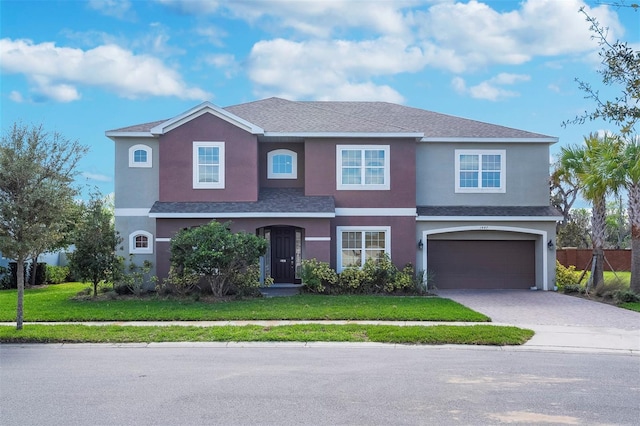 traditional home featuring a garage, decorative driveway, a front yard, and stucco siding