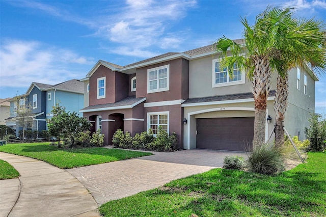 traditional home with an attached garage, a front lawn, decorative driveway, and stucco siding