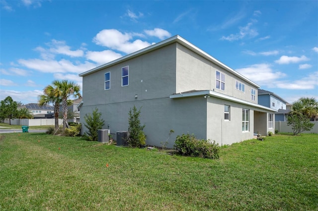 view of side of property featuring fence, a lawn, central AC, and stucco siding