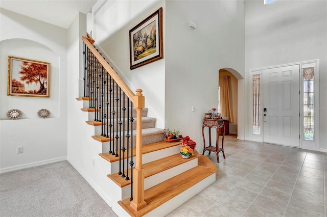 foyer featuring baseboards, arched walkways, stairway, tile patterned floors, and a high ceiling