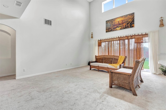 sitting room with arched walkways, a high ceiling, carpet, and visible vents