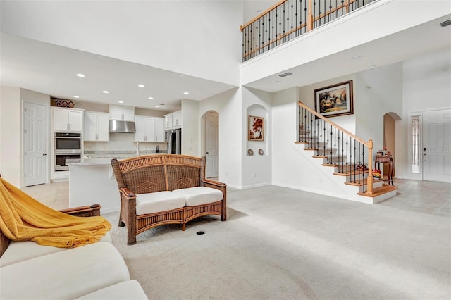 living room featuring arched walkways, light carpet, a high ceiling, and stairs